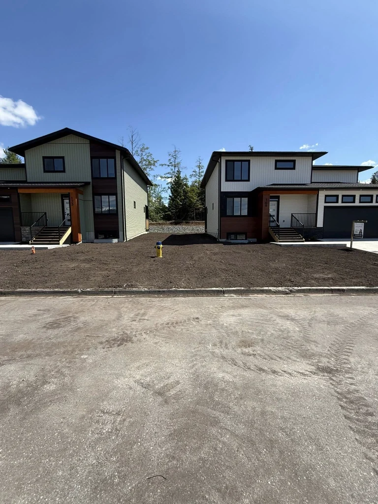 Front view of two new houses with rough graded lots and compacted soil prepared for finishing work in a residential development.