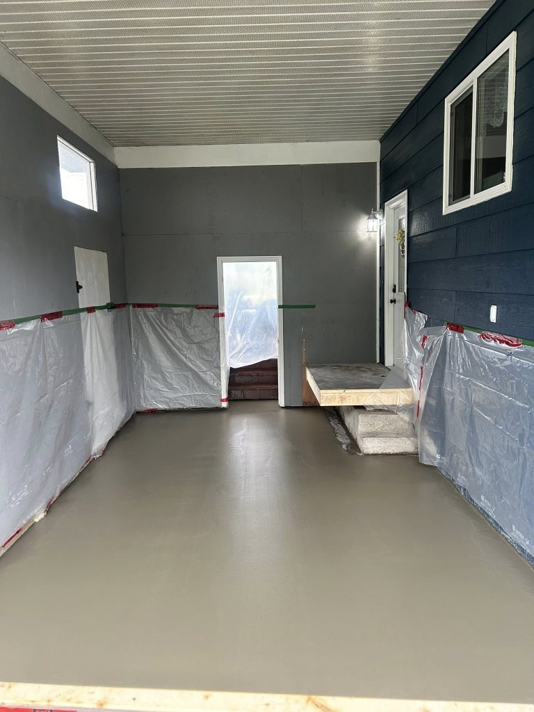 Interior room with freshly finished concrete floor and lower walls protected with plastic sheeting.