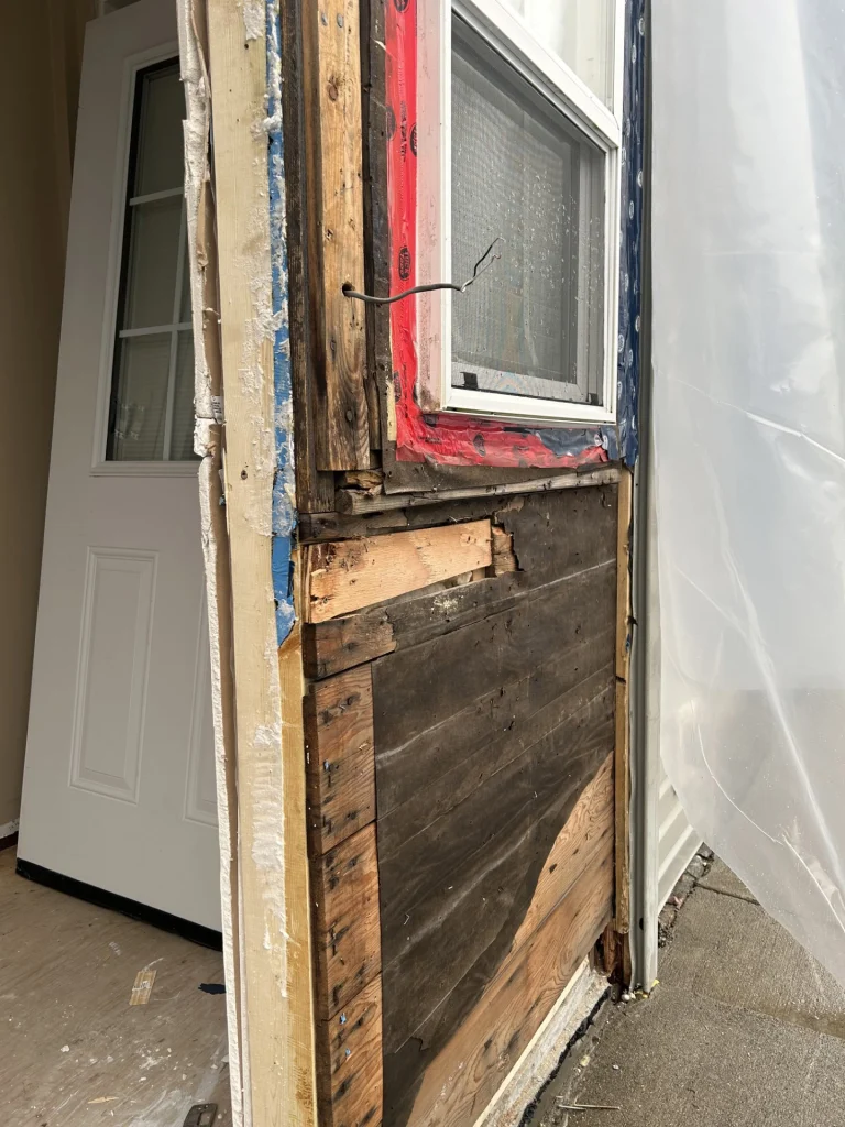Exterior wall opened to show water damage and structural repair area around door and window
