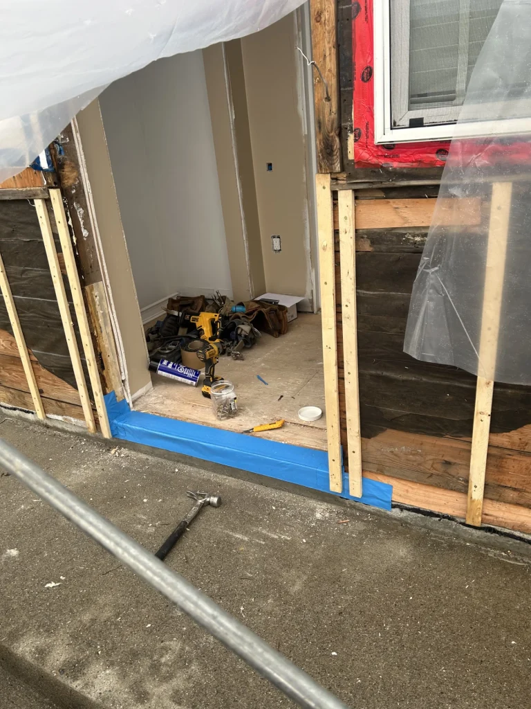 Exterior renovation in progress with wall framing and waterproofing repairs at entryway