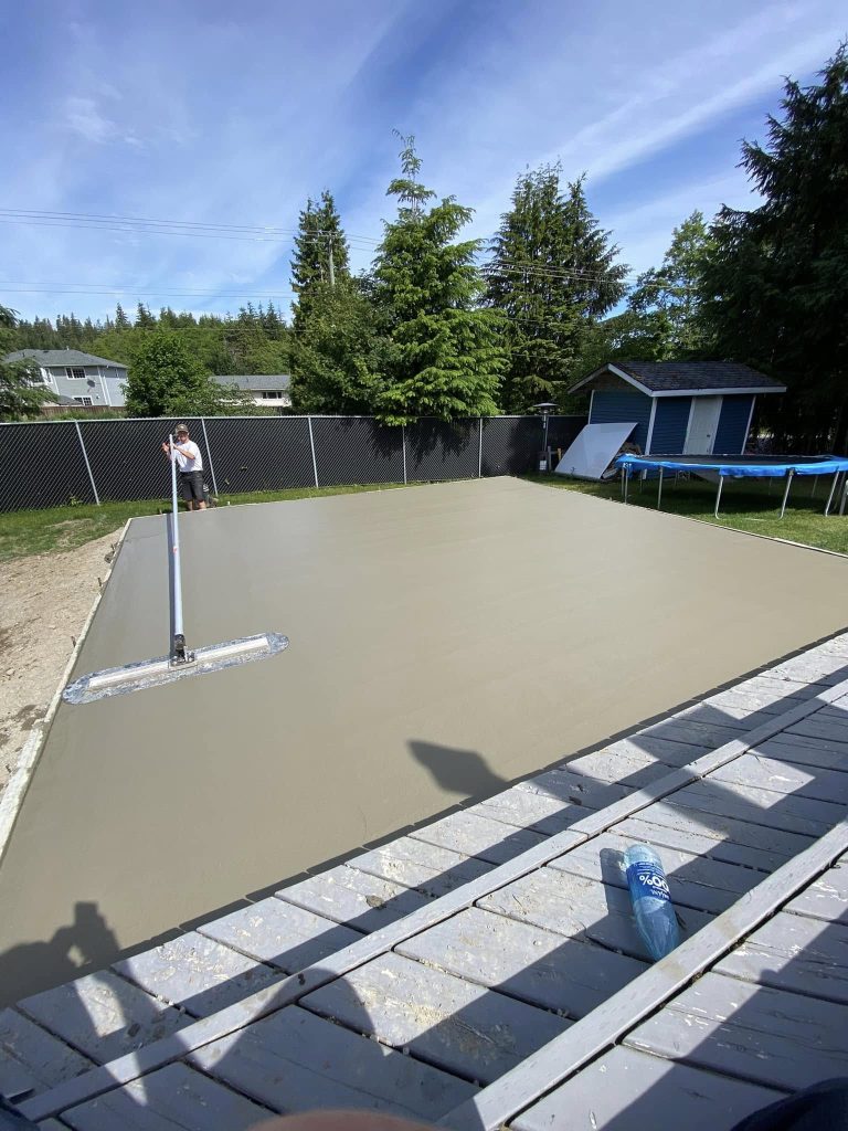 Fresh concrete slab being leveled and finished in a residential backyard.
